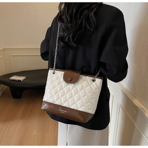 Detail of quilted white bucket bag with contrast brown trim and chain strap on model