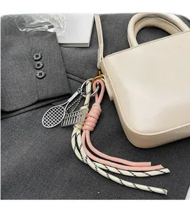 Detail of mini tennis racket and abacus charm with woven tassel on beige leather handbag