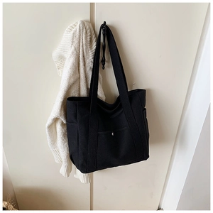 Detail view of black canvas tote bag with side pockets and functional metal snap button