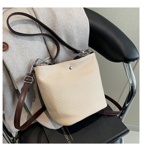 Gros plan sur un sac seau tissé beige avec texture à chevrons et bandoulière en cuir brun