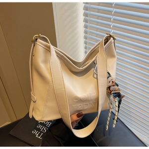 Close-up of cream shoulder bag featuring embossed lettering and a cute bear charm accessory