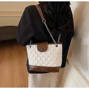 Detailed view of quilted white and brown bucket bag with chain strap worn by a model