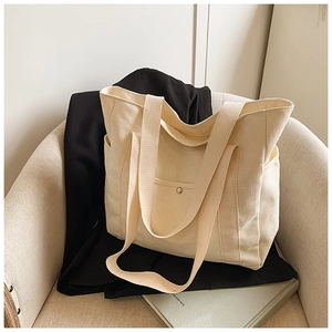 Detail view of cream canvas tote bag with front pocket and wide shoulder straps