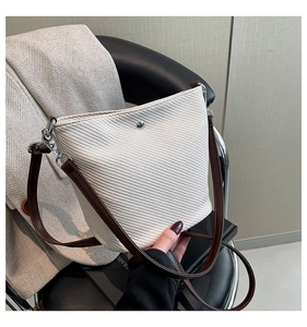 Détail du sac seau tissé crème montrant le fermoir argenté et la bandoulière en cuir brun
