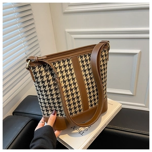 Detailed view of houndstooth bucket bag with brown leather trim in a minimalist setting