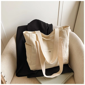 Detail of a minimalist cream canvas tote bag with front snap pocket on a sofa