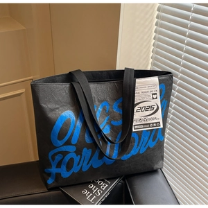 Détail du grand sac cabas noir texturé avec texte bleu et grand écusson blanc