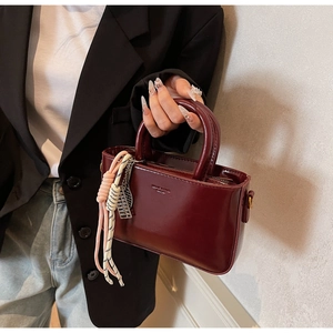 Detail of burgundy vintage handbag with woven charm and textured leather surface