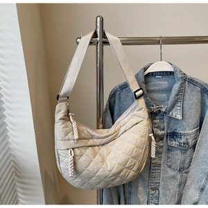 Close-up of beige quilted crescent bag with adjustable wide strap and rope zipper pull