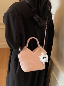 Élégant sac seau rose avec breloque peluche, porté avec un blazer noir pour un look chic