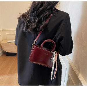Close-up of a burgundy glossy leather handbag with woven rope charm on a black suit