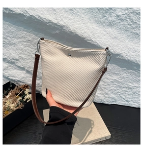 Gros plan du sac seau tressé crème avec bandoulière en cuir marron et boucle en métal argenté