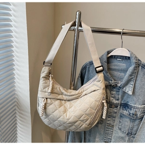 Close-up of beige quilted half-moon shoulder bag with metal zipper and woven puller