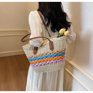 Detail of hand-woven straw tote bag with colorful braided straps and leather handles