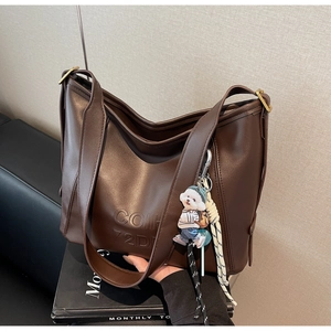 Detail of dark brown tote bag with embossed letters and cute doll charm accessory