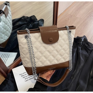 Detail view of quilted beige bucket bag with dark brown trim and silver chain strap