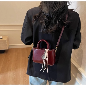Detail of burgundy leather mini bag with silver tennis racket charm and woven tassel