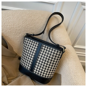 Détail du sac seau en pied-de-poule avec bordure en cuir noir et surpiqûres sur la bandoulière