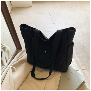 Close-up of black canvas tote bag featuring front pocket with metal buckle and side storage