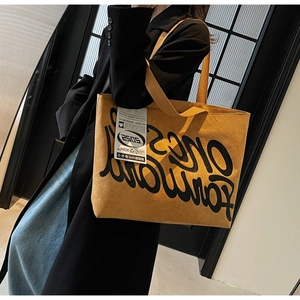 Détail du grand sac cabas en cuir jaune gingembre avec lettres noires et étiquette textile