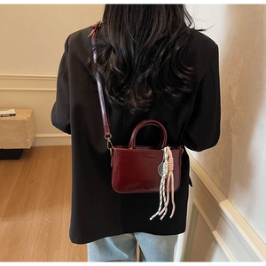 Close-up of a burgundy patent leather handbag featuring a tennis racket charm detail