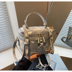 Détail du sac boîte argenté avec ferrures dorées, breloques et ruban en soie