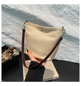 Détail du sac seau tissé crème avec bandoulière en cuir marron et boucle en métal