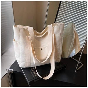 Detailed texture of off-white canvas tote bag featuring front pocket with metal snap button