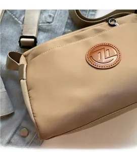 Détail du sac bandoulière kaki avec logo en cuir sur un tissu en nylon doux et souple