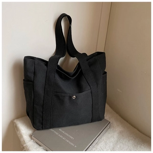 Detail of black canvas tote bag showing front pocket with silver snap and side pouch