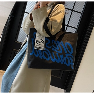 Détail d'un grand sac cabas noir avec lettres graffiti bleues et texture chic