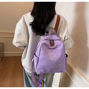 Detail of lavender nylon backpack with cat embroidery and leather handles on model