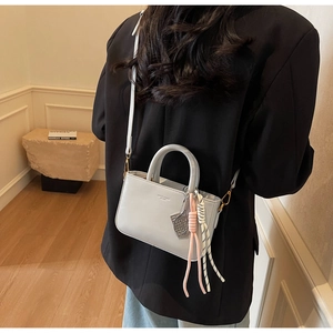 Detail of light blue-grey square handbag with tennis racket charm and crossbody strap