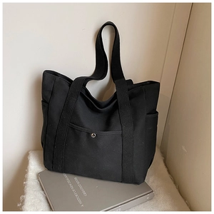 Detail of black canvas tote bag showing the front pocket with metal snap fastener