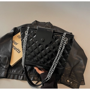 Close-up of black quilted chain tote bag in glossy leather finish on modern desk