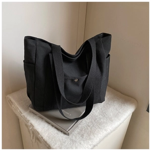 Detail view of black canvas tote bag showing wide shoulder straps and front buckle pocket