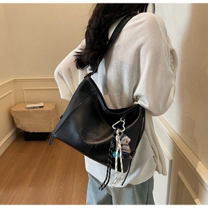 Detail of black leather hobo bag featuring a cute bear charm and woven rope strap