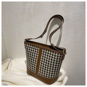 Close-up of houndstooth fabric texture and brown leather trim on the bucket bag