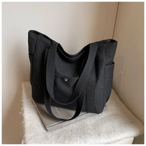 Close-up of black canvas tote bag showing front pocket with silver metal snap button