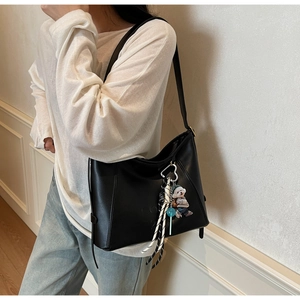 Detail of black leather shoulder bag with a cute striped dog charm and woven strap accessory