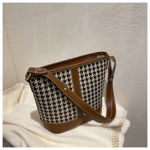Detail of houndstooth bucket bag featuring dark brown leather trim and golden hardware