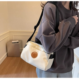 Détail du sac bandoulière blanc cassé avec logo rond et sangle noire réglable