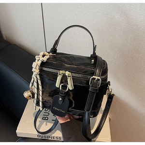 Détail d'un sac boîte noir brillant avec clochette dorée et bandoulière réglable