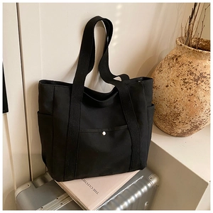 Detailed side pocket and silver magnetic clasp on a durable black canvas tote bag