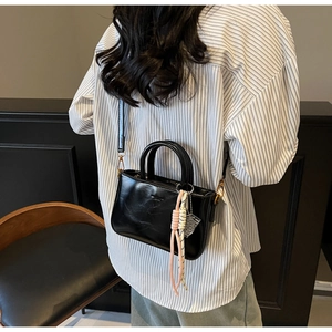 Detail of vintage black oil wax leather handbag with braided charm shown on model
