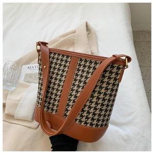 Detail of houndstooth bucket bag with brown leather trim and thin shoulder strap