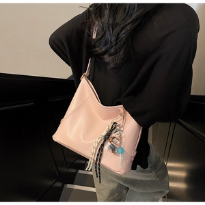 Close-up of pink faux leather bucket bag with teddy bear pendant and woven charm detail