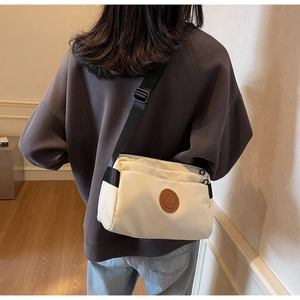 Détail du sac bandoulière crème avec écusson logo et large bandoulière ajustable