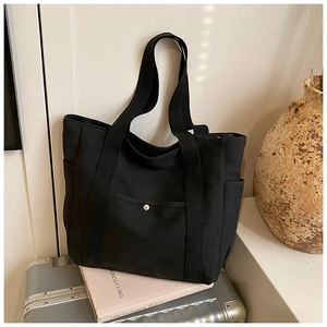 Close-up of black canvas tote bag showing side pockets and silver button pocket detail