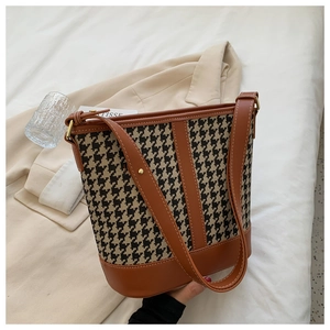 Close-up of houndstooth fabric bucket bag with dark brown leather trim and shoulder strap